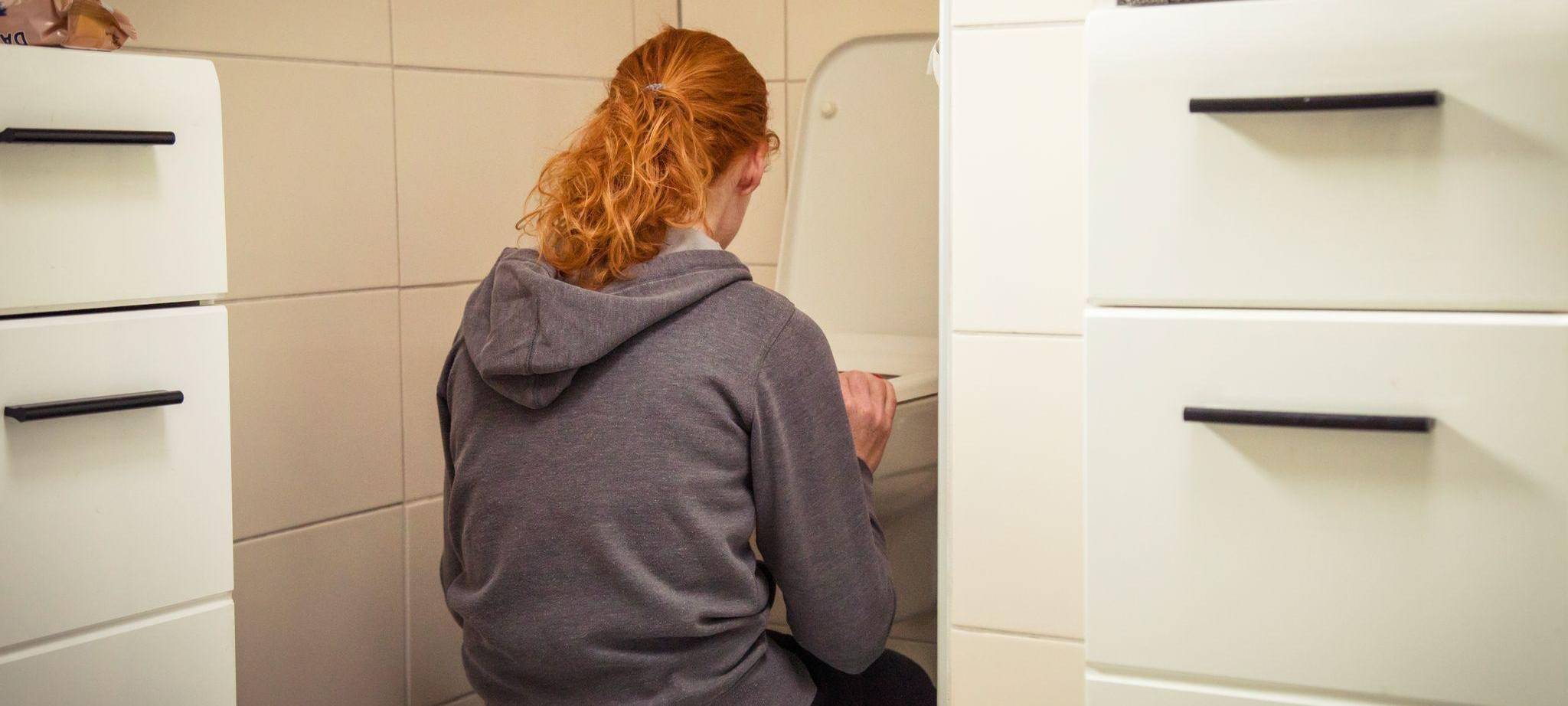 Frau hockt vor einer Toilette im Badezimmer