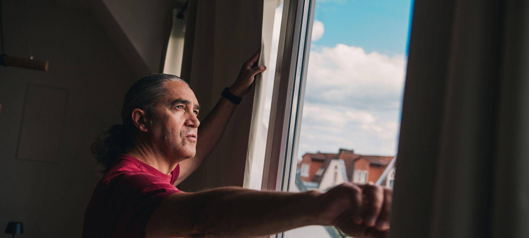 Mann steht vor dem Fenster seiner Wohnung