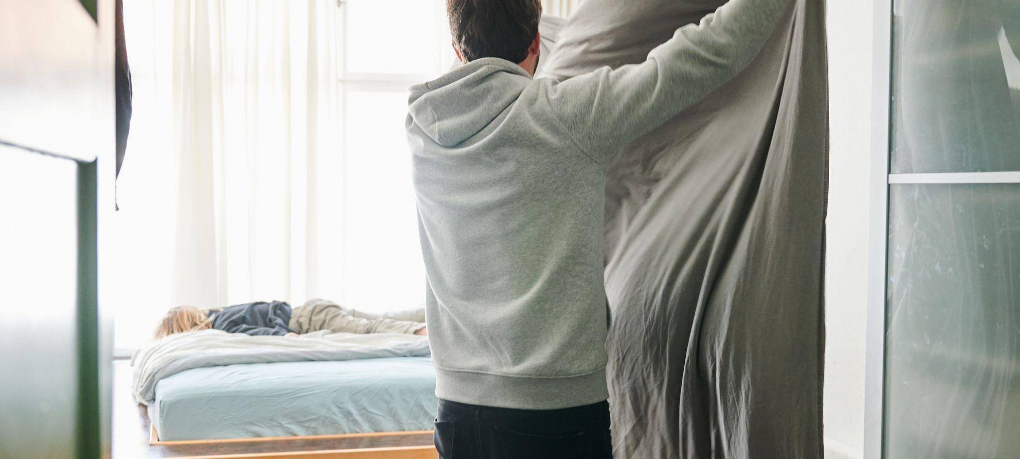 Ein Mann bezieht das Bett und schüttelt dabei eine Bettdecke