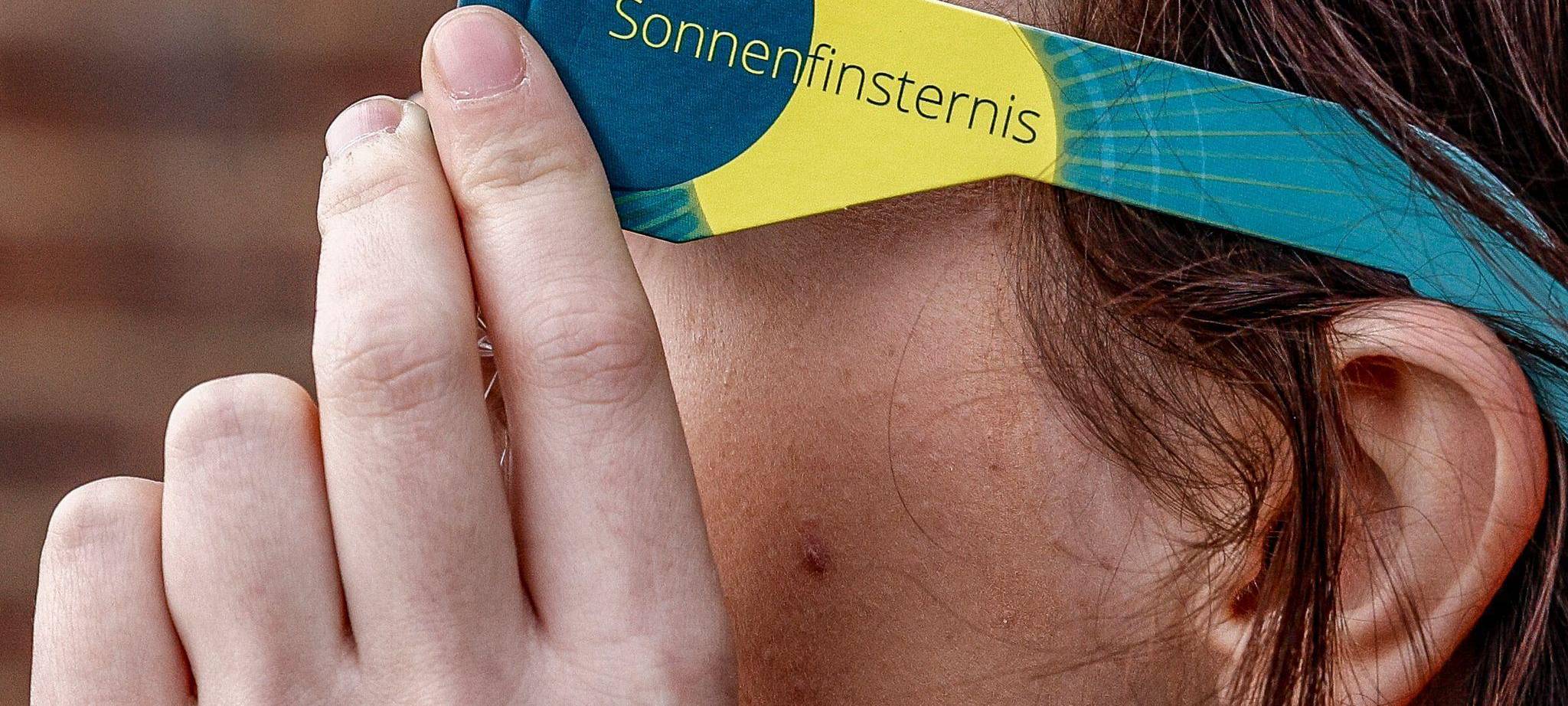 Frau mit Schutzbrille betrachtet eine partielle Sonnenfinsternis